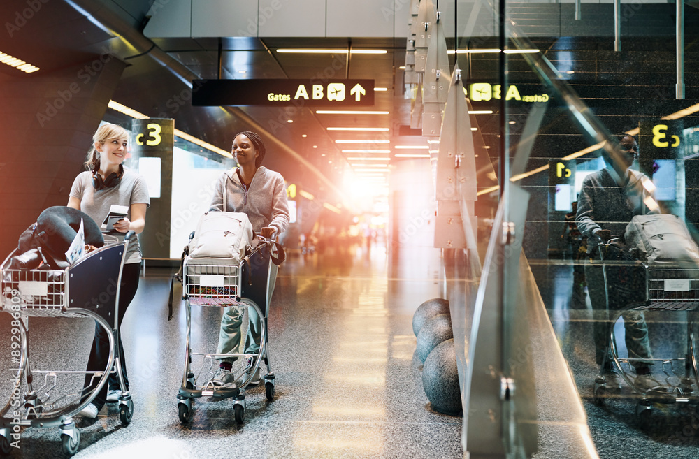 Naklejka premium Travel, friends and women at airport with luggage trolley for vacation, holiday or trip together. Walking, suitcase or happy girls at airline with passport for journey, talk or arrival at flight gate