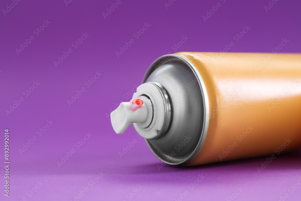 Orange spray paint can on violet background, closeup. Space for text Orange spray paint can on violet background, closeup. Space for text