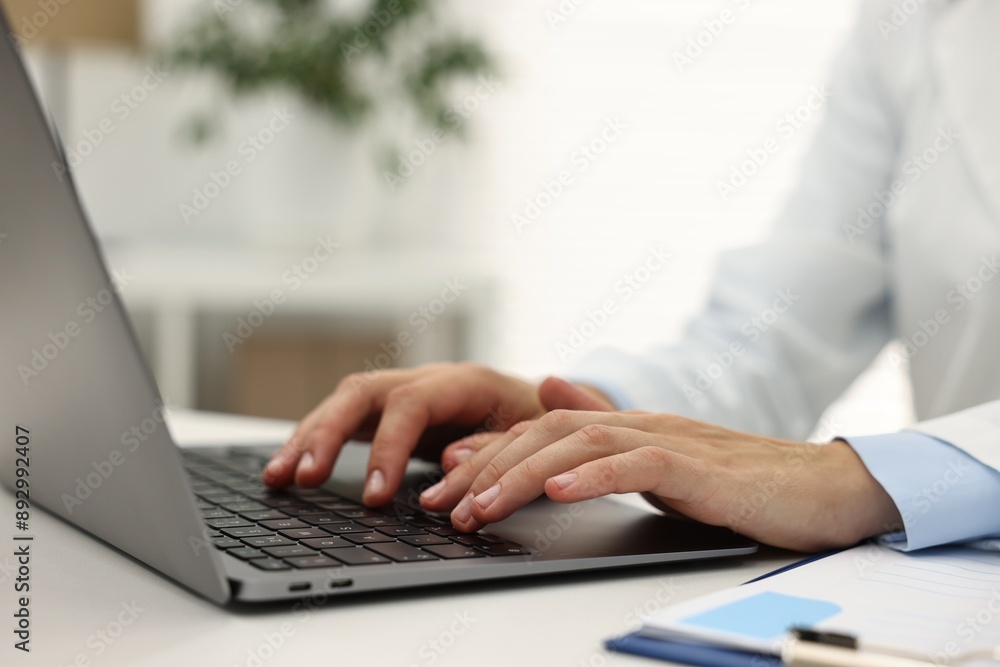 Doctor using laptop at white table in hospital, closeup Doctor using laptop at white table in hospital, closeup