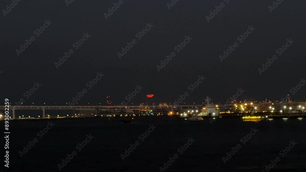 A bridge and cityscape illuminated at night with a red moon rising in the background A bridge and cityscape illuminated at night with a red moon rising in the background