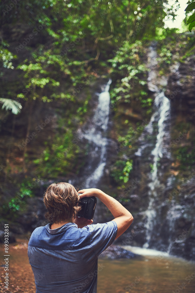 Fototapeta premium Man, camera and photographer by waterfall in nature for photography, rainforest and environment picture of travel. Back, male person and digital gear for creative adventure, exploring and memory
