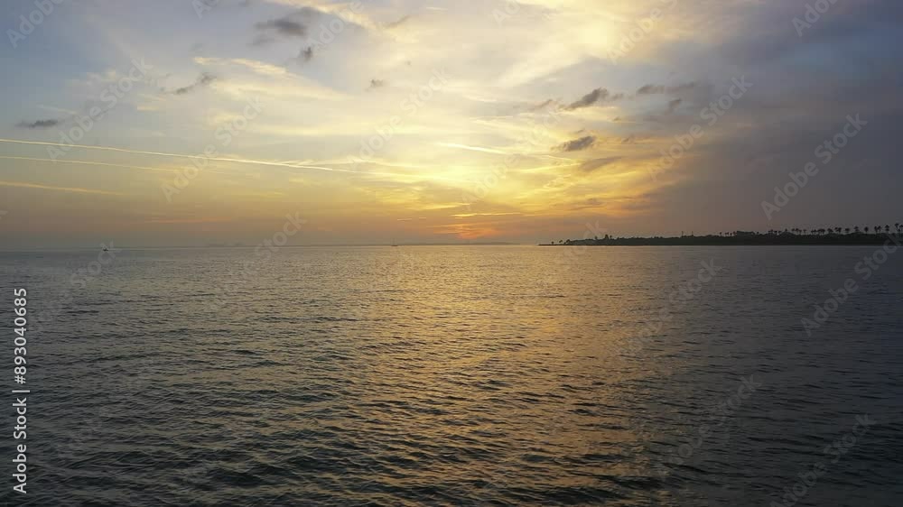 Aerial view of a drone flying across calm waters during a beautiful sunset, with a scenic coastline and palm trees in the distance. Aerial view of a drone flying across calm waters during a beautiful sunset, with a scenic coastline and palm trees in the distance.