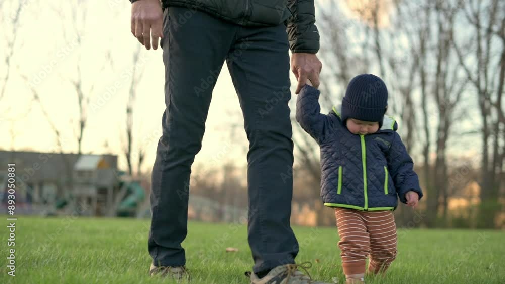 A joyful toddler walks hand in hand with an adult through a grassy park, smiling and enjoying the moment. The video captures the warmth and happiness of a family outing on a sunny day. A joyful toddler walks hand in hand with an adult through a grassy park, smiling and enjoying the moment. The video captures the warmth and happiness of a family outing on a sunny day.