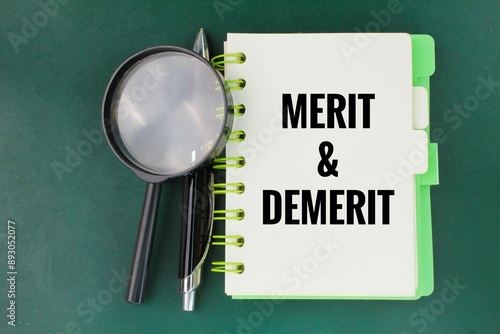 a pen, a magnifying glass and a book with the words MERIT and DEMERIT. Merits refer to the advantages. Demerits refer to the unfavorable points of something photo