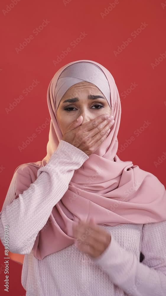 Vertical video. Frightened face. Omg panic. Shocking news. Scared speechless worried woman in hijab covering mouth isolated on red copy space background. Vertical video. Frightened face. Omg panic. Shocking news. Scared speechless worried woman in hijab covering mouth isolated on red copy space background.