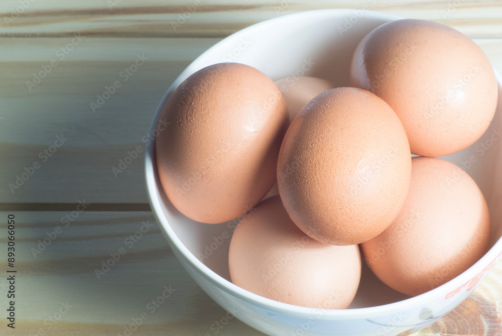Close-up image raw chicken eggs in a white bowl on wooden table, horizontal view. Close-up image raw chicken eggs in a white bowl on wooden table, horizontal view.