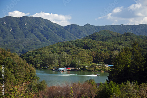 Nam-myeon, Chuncheon-si, Gangwon-do, South Korea - October 5, 2010: Summer view of a tourist riding water ski with motorboat on Cheongpyeong Lake against mountain
 photo