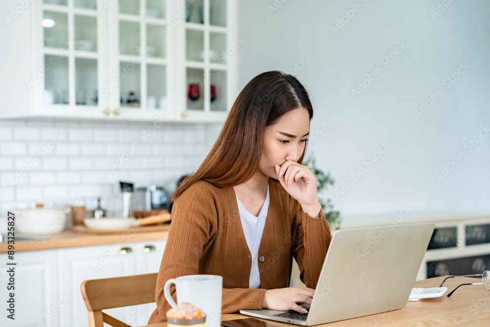Asian young woman seriously working on computer laptop in house. She thinking find solution problem of work Asian young woman seriously working on computer laptop in house. She thinking find solution problem of work