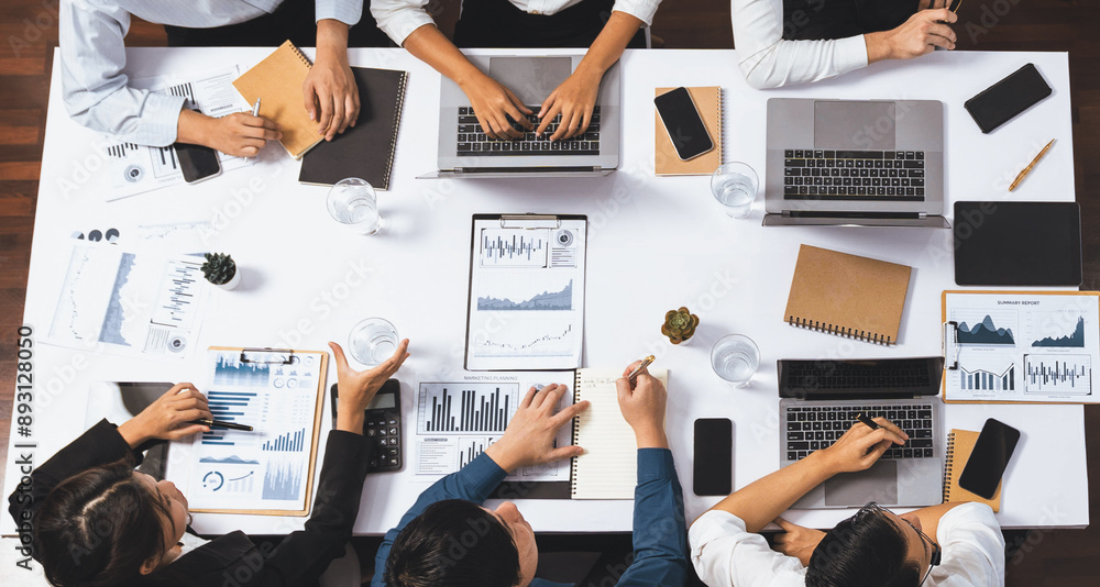 Obraz premium Top view analyst team utilizing BI Fintech to analyze financial data at table in meeting room. Analytic BI dashboard power on paper for business insight and strategic marketing planning. Prudent