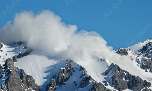 A large avalanche rolls down a snow-covered mountain peak on a bright, sunny day. Natural disaster photo