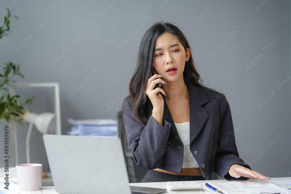 Focused young asian businesswoman in modern office multitasking on laptop and phone call, feeling pressure of looming deadline Focused young asian businesswoman in modern office multitasking on laptop and phone call, feeling pressure of looming deadline