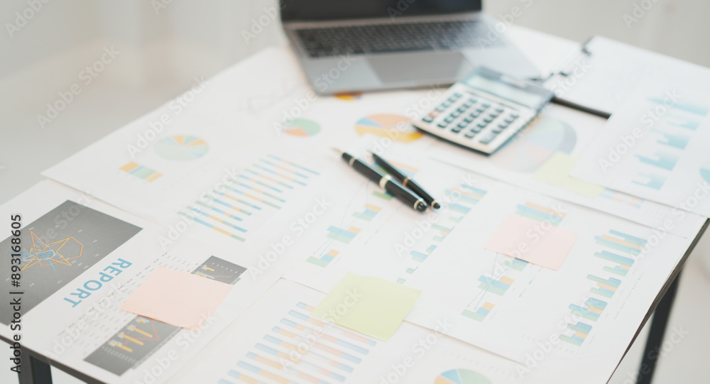 An office desk with laptop, calculator and documents showing the reports, graphs and charts for the business meeting An office desk with laptop, calculator and documents showing the reports, graphs and charts for the business meeting