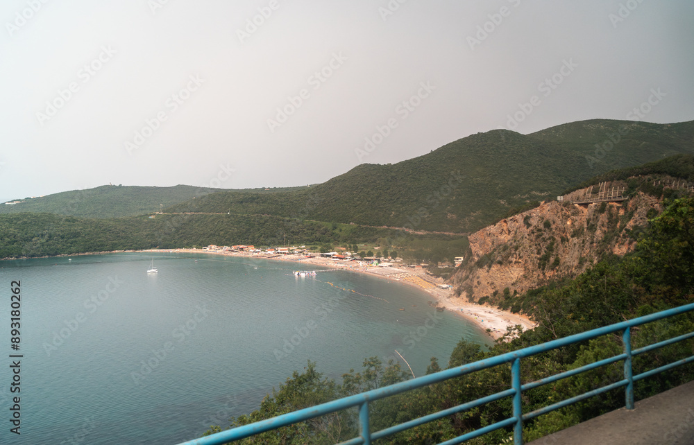 Beach view in Budva, Montenegro. Sandy pebbles shore with umbrellas, beachgoers, and water activities
