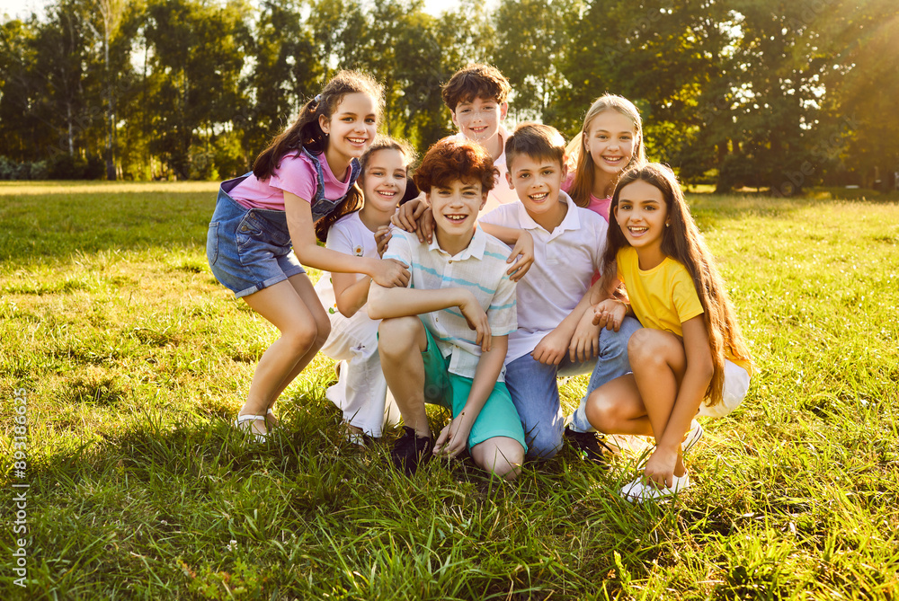 Fototapeta premium Happy children friends standing together outdoors, having fun and smiling in the park on holidays enjoying spending time in a summer camp. Portrait of a kids looking at camera on the lawn in nature.