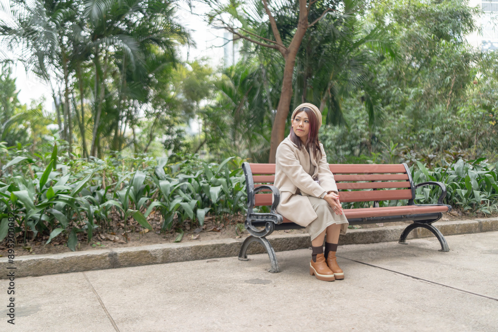 Thirty-something Hong Kong woman with reddish-brown hair sitting on a bench by a large fountain in Kowloon Park, Tsim Sha Tsui, Kowloon Island, Hong Kong, during a cold winter. Thirty-something Hong Kong woman with reddish-brown hair sitting on a bench by a large fountain in Kowloon Park, Tsim Sha Tsui, Kowloon Island, Hong Kong, during a cold winter.