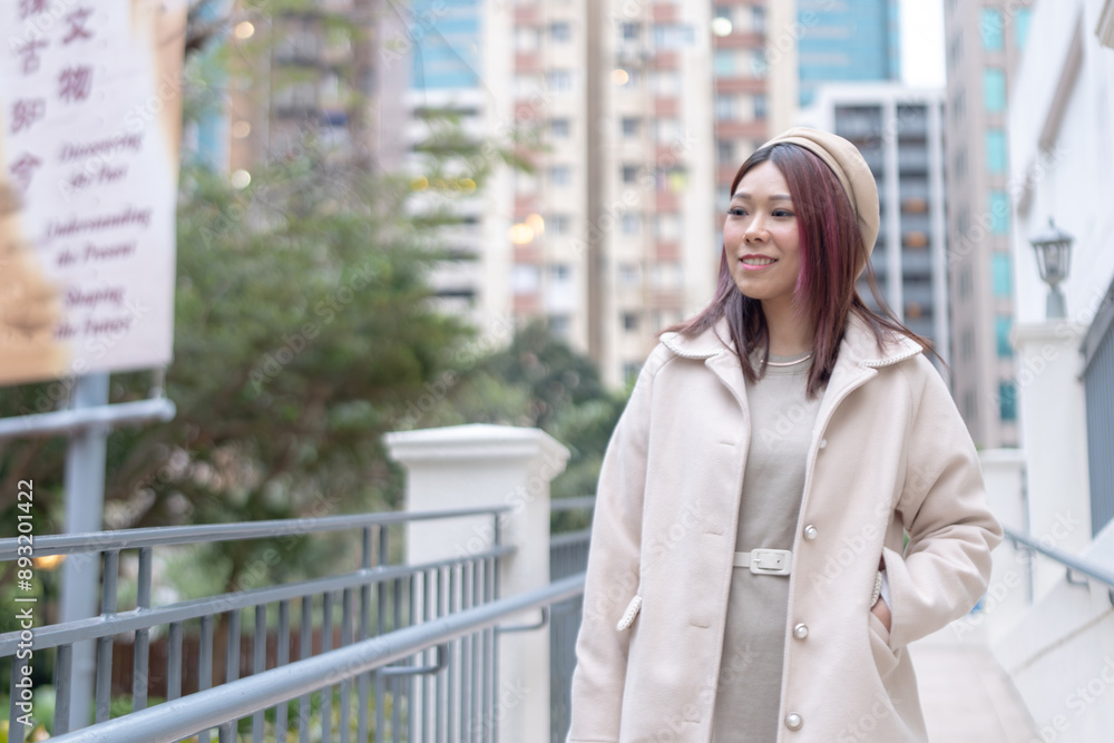 Thirty-something Hong Kong woman with reddish-brown hair walking by a large fountain in Kowloon Park, Tsim Sha Tsui, Kowloon Island, Hong Kong, during a cold winter. Thirty-something Hong Kong woman with reddish-brown hair walking by a large fountain in Kowloon Park, Tsim Sha Tsui, Kowloon Island, Hong Kong, during a cold winter.