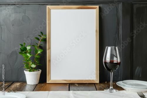 Empty wooden frame mockup with a potted plant and a glass of red wine on a rustic table against a dark background. Perfect for showcasing art or s.