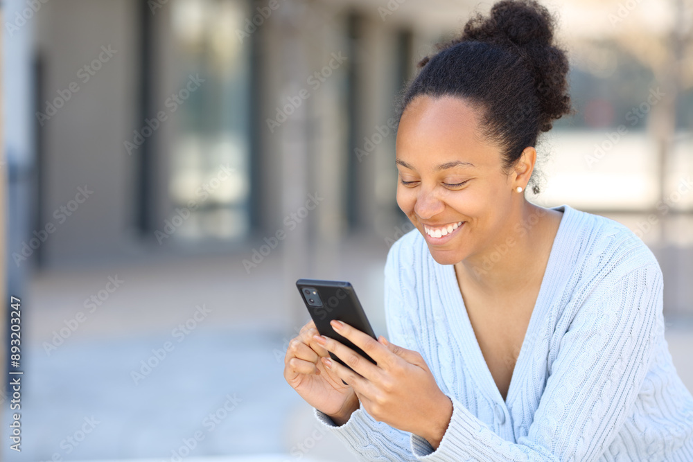 Happy black woman using cell phone sitting in the street Happy black woman using cell phone sitting in the street
