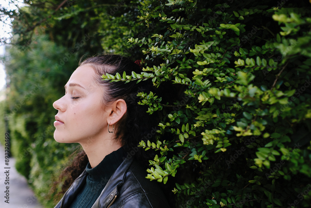 Beautiful young woman with eyes closed standing by green plants Beautiful young woman with eyes closed standing by green plants