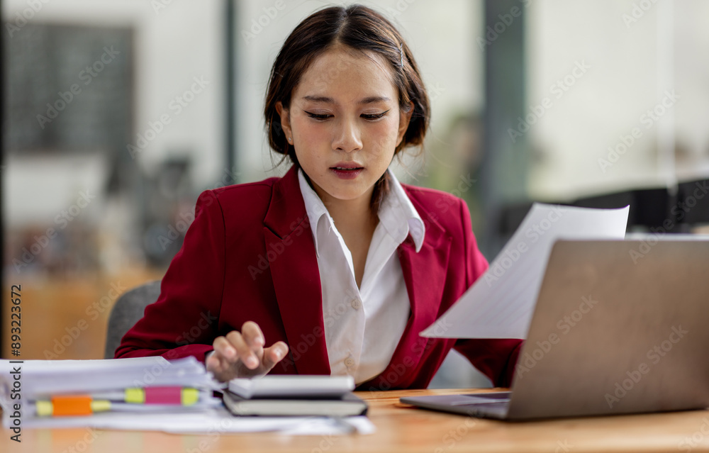 Serious and focused financial accounting on documents paper work at office, Asian woman use calculator and laptop for calculating reports and summarizing accounts, business at work in casual clothes. Serious and focused financial accounting on documents paper work at office, Asian woman use calculator and laptop for calculating reports and summarizing accounts, business at work in casual clothes.
