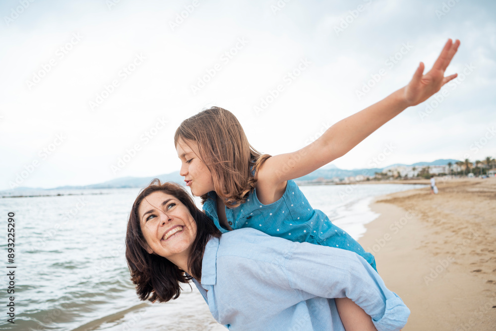 Cheerful mother giving piggyback ride to daughter at beach Cheerful mother giving piggyback ride to daughter at beach