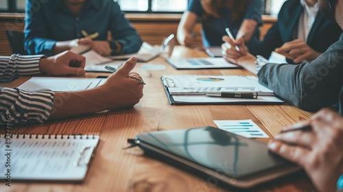 A team meeting with the boss leading the discussion, employees taking notes in their notebooks, a whiteboard filled with plans and schedules, and everyone dressed in professional attire