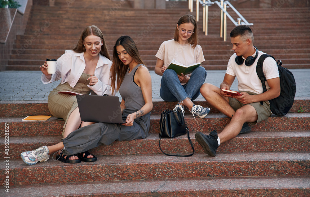Fototapeta premium Relaxed, on the stairs, with laptop. Group of students are outside together