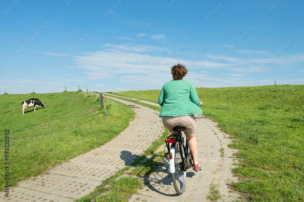 Woman riding bicycle on road amidst field under sky Woman riding bicycle on road amidst field under sky