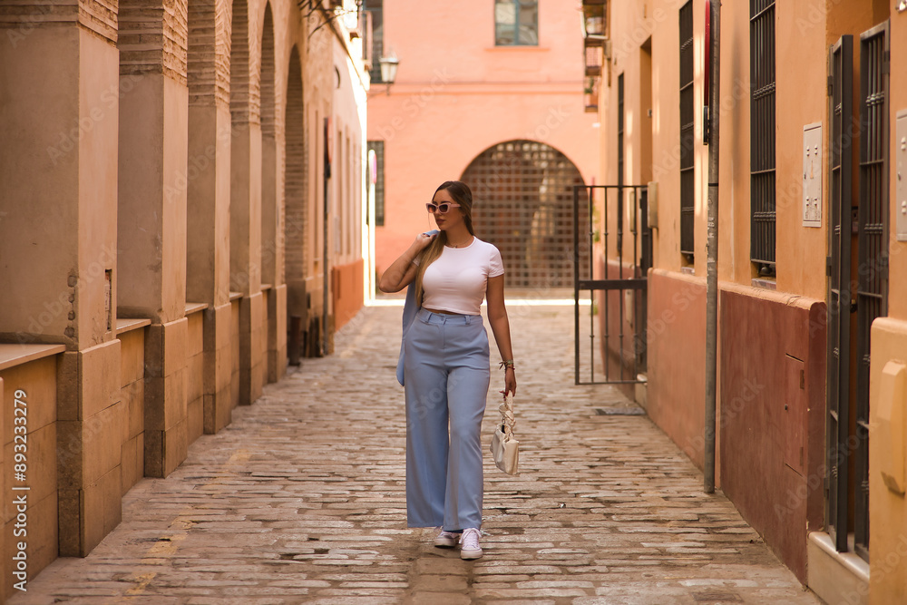 Young beautiful woman with brown hair, sunglasses and blue jacket suit, walking with jacket over her shoulder on a lonely street. Concept beauty, fashion, trend. Young beautiful woman with brown hair, sunglasses and blue jacket suit, walking with jacket over her shoulder on a lonely street. Concept beauty, fashion, trend.