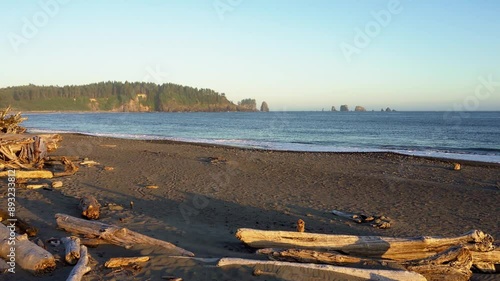 Pan right of La Push Beach at sunset with driftwood scattered along the pebbled shore and a forested coastline in the background. 4K UHD video.