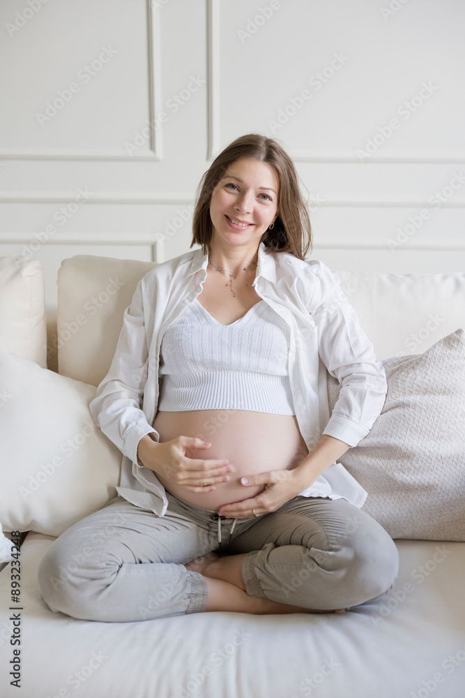 Smiling pregnant woman with hands on belly sitting cross-legged at home Smiling pregnant woman with hands on belly sitting cross-legged at home