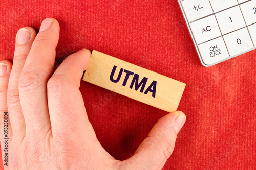 UTMA - Uniform Transfers to Minors on wooden blocks with a hand, part of a calculator on a red background photo