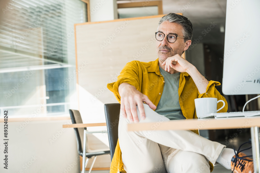 Thoughtful businessman sitting with coffee cup at desk Thoughtful businessman sitting with coffee cup at desk