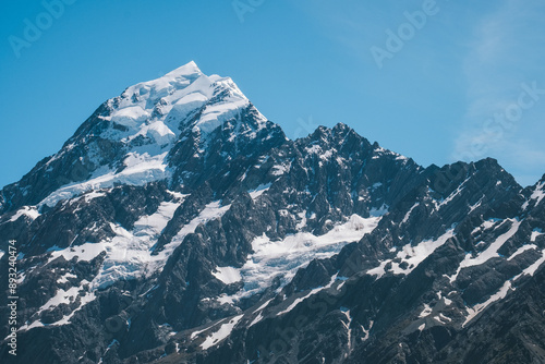 A close-up view of the snow-capped peak of Mount Cook, showcasing its rugged and majestic features. The pristine snow and clear blue sky highlight the beauty and grandeur of this iconic mountain in H