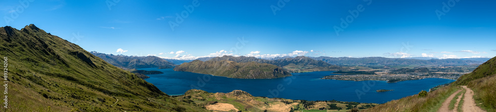 Obraz premium A panoramic view of a mountain and lake landscape, highlighting the vastness and beauty of the natural environment. The clear blue sky and expansive scenery create a tranquil and inviting atmosphere.