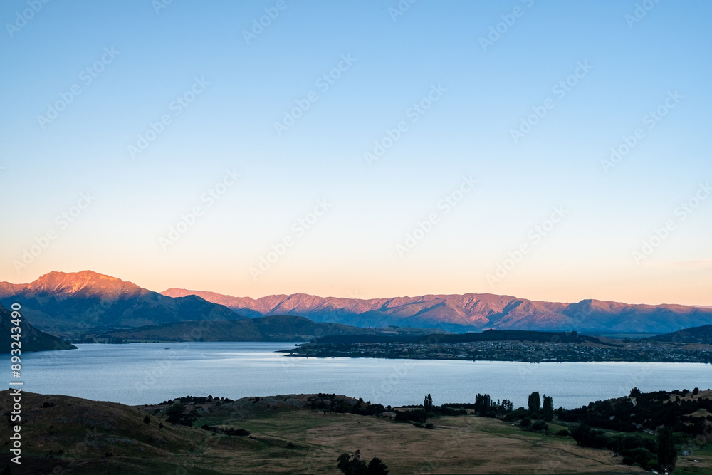 Fototapeta premium The sun sets over a mountain lake, casting a warm glow over the serene landscape and creating a peaceful, picturesque scene.