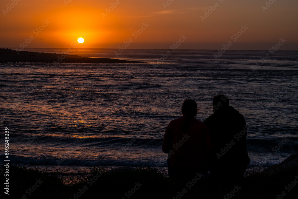 A beautiful sunset on the beach with silhouettes of people enjoying the view, the sky glowing with warm hues, and the ocean waves gently rolling.