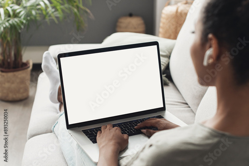 Young woman using laptop computer at home. Blank empty white screen mock up. Freelance, student lifestyle, education, web conference, video call, technology and online shopping concept photo