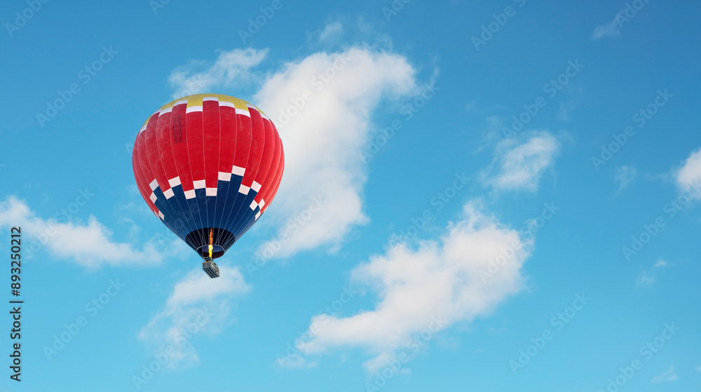 Fototapeta premium Hot air balloon in dark blue, red and yellow colors flying in a slightly cloudy blue sky