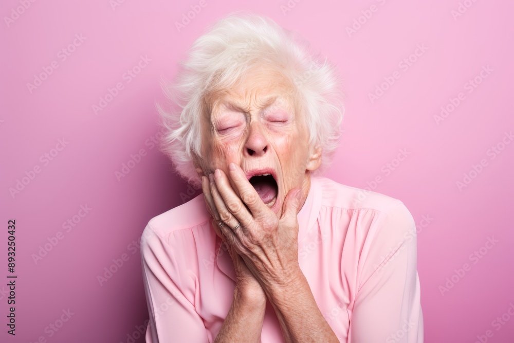 Photo of a close-up portrait of a 70-year-old woman, Caucasian, yawning sweetly with her hand covering her mouth on a pastel light pink background
Photo of a close-up portrait of a 70-year-old woman, Caucasian, yawning sweetly with her hand covering her mouth on a pastel light pink background
