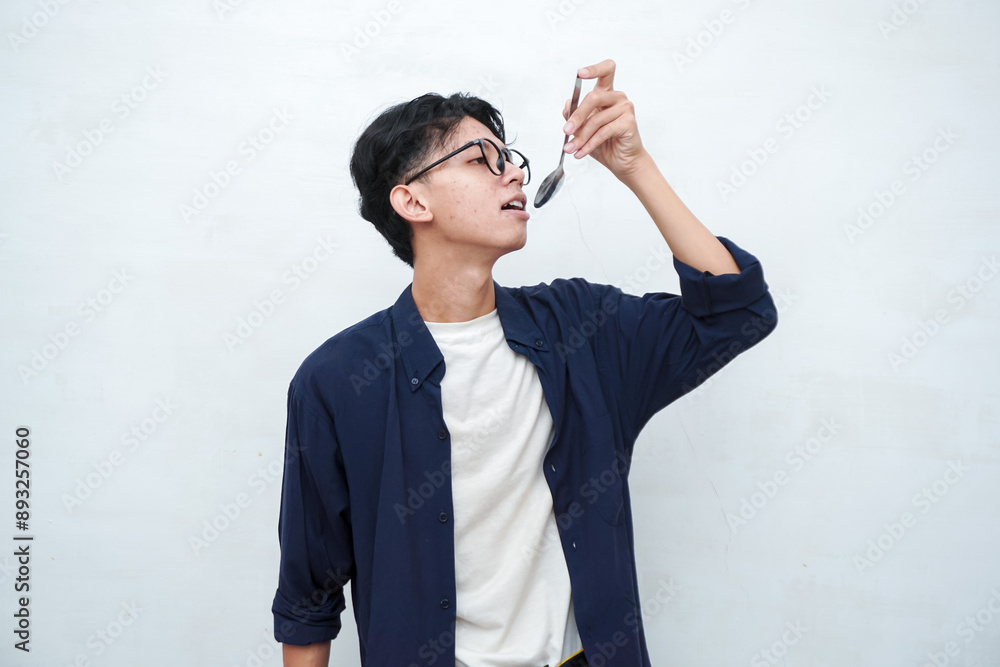 Young Asian man holding spoon and showing eating gesture. Asian man with blue shirt eating food, isolated on white background. Eating medicine with spoon Young Asian man holding spoon and showing eating gesture. Asian man with blue shirt eating food, isolated on white background. Eating medicine with spoon
