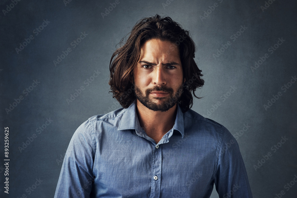 Obraz premium Serious man, portrait and fashion with hairstyle, beard or frown for attitude on a gray studio background. Handsome male person or young model with facial expression, aggression or casual tshirt