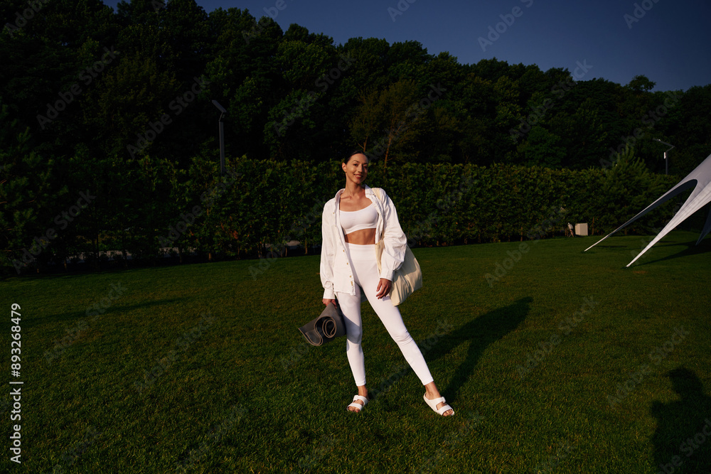 Obraz premium Happy smiling woman is standing on the green grass, trees at background