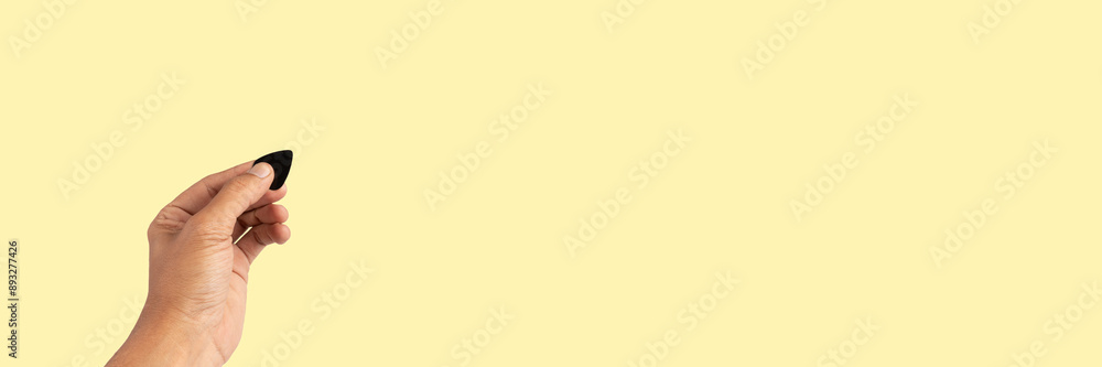 Male hand holding a guitar pick isolated on yellow background banner Male hand holding a guitar pick isolated on yellow background banner