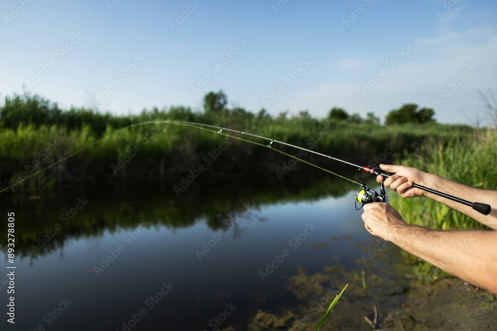 Man catching fish, pulling rod while fishing from lake or pond. Fisherman with rod, spinning reel on river bank. Man catching fish, pulling rod while fishing from lake or pond. Fisherman with rod, spinning reel on river bank.