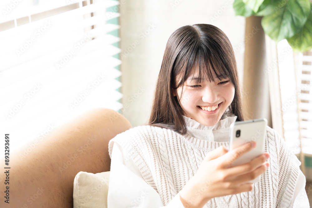 部屋でスマホを見ながら笑っている女の子 部屋でスマホを見ながら笑っている女の子
