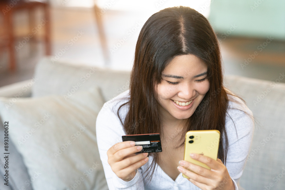 ソファに座ってスマホでカード決済をしている女性 ソファに座ってスマホでカード決済をしている女性