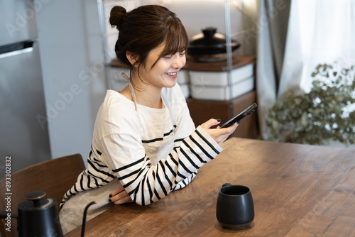 ダイニングに座ってスマホを笑顔で見ている女性 photo