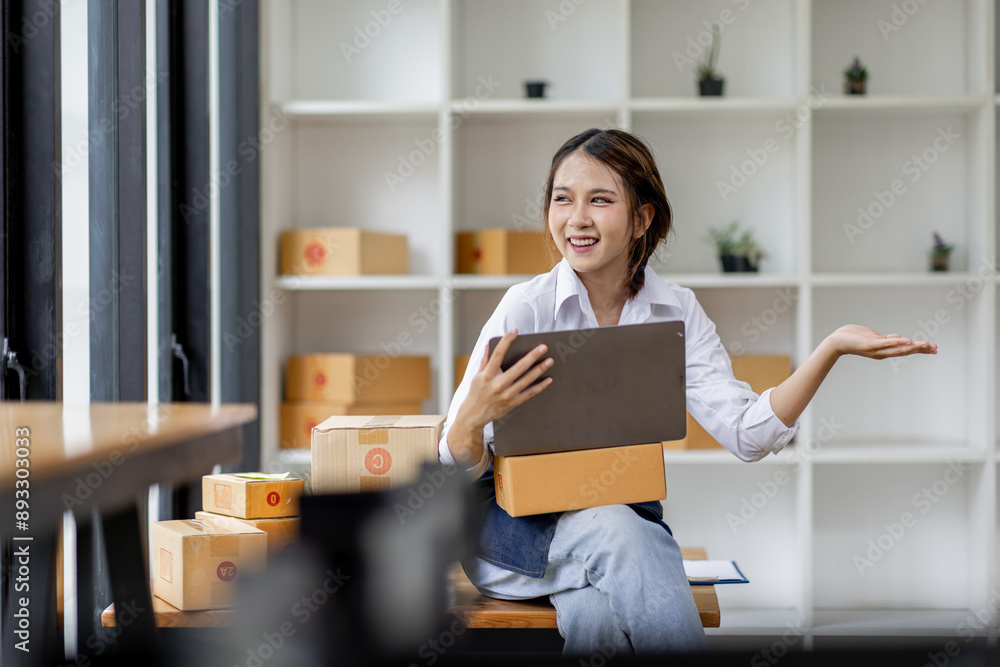 Portrait business woman smile and use laptop checking information on parcel shipping box before send to customer. Entrepreneur small business working at home. SME business online marketing. Portrait business woman smile and use laptop checking information on parcel shipping box before send to customer. Entrepreneur small business working at home. SME business online marketing.