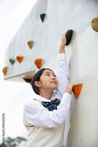 ボルダリングの壁を登っている制服姿の女子学生